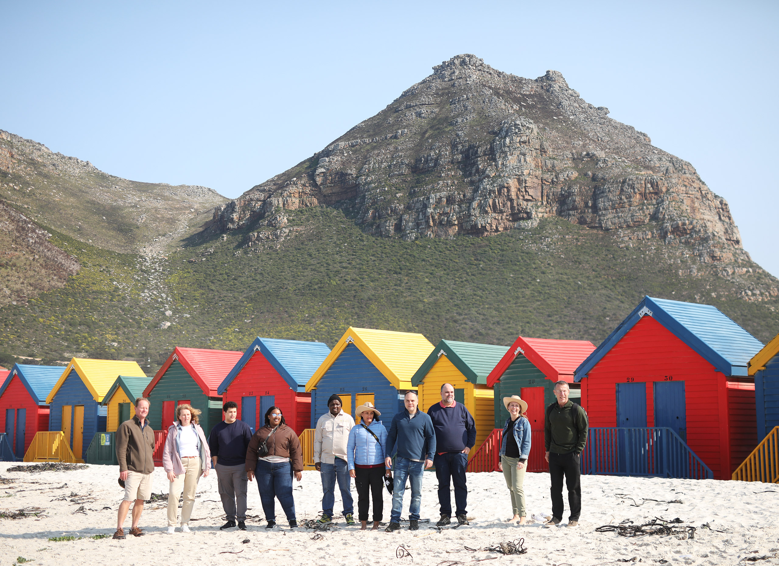 A group of people standing in front of colourful houses in Muizenberg.